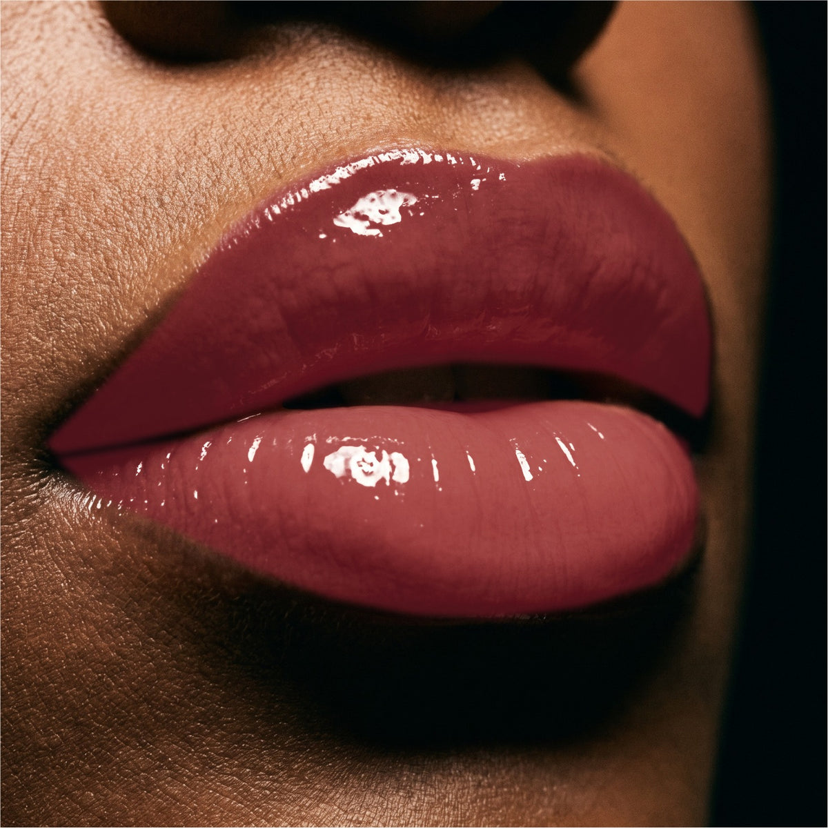 Close-up of glossy Cherry Cola  lips wearing a high-shine lip gloss or lip gloss, with dark skin tones and a black background.