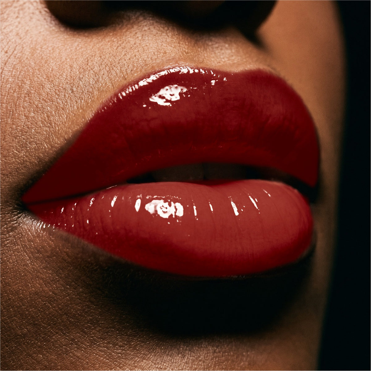 Close-up of glossy deep red lipstick on a person's lips against a dark background.