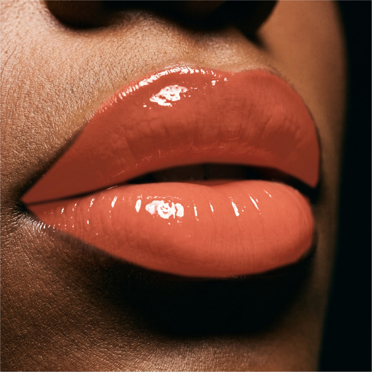 Close-up of glossy Mango lipstick on a person's lips against a dark background.