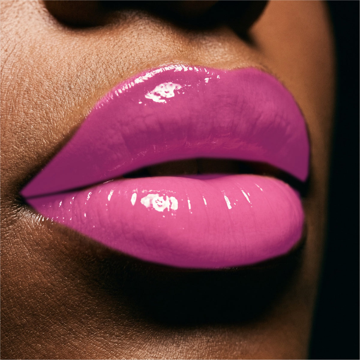 Close-up of glossy Pink Punch lip gloss on a person's lips against dark skin tones and a black background.