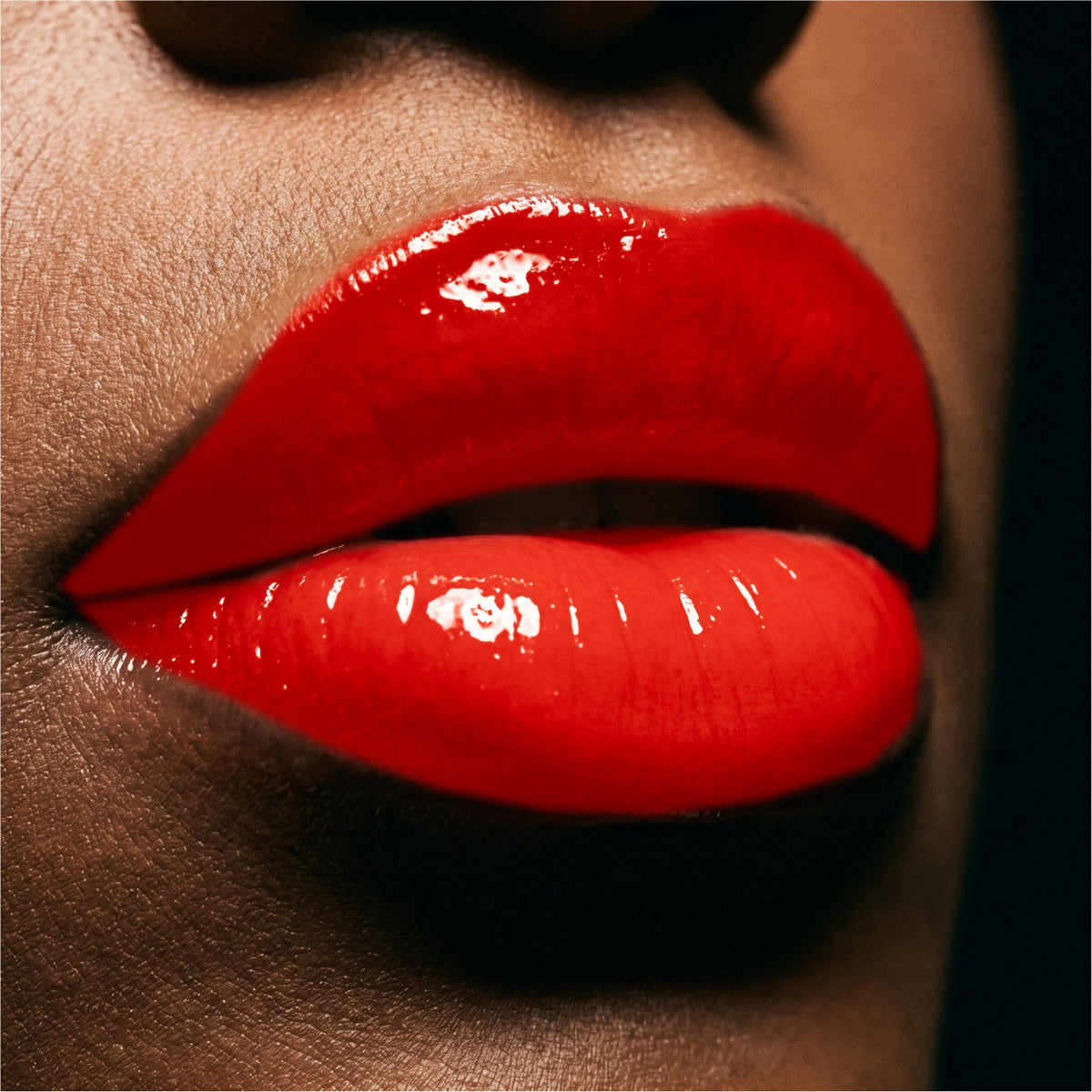 Close-up of glossy Ruby Red lipstick on a person's lips against a dark background.